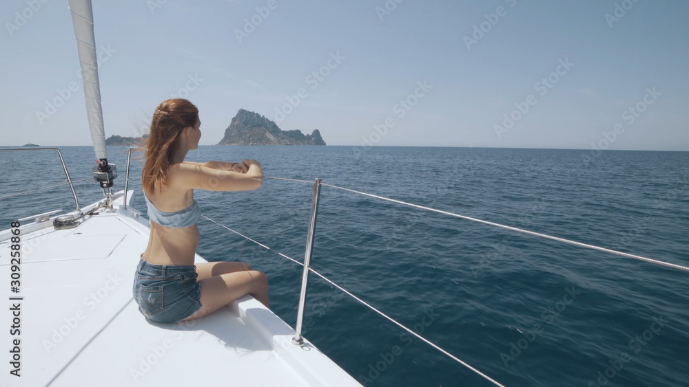 Obraz premium Beautiful woman on a yacht enjoys the journey on the background of the islands of Ibiza or Mallorca. Luxury yacht near the balearic islands
