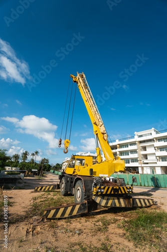 Yellow automobile crane with risen telescopic boom outdoors. Mobile construction crane on a constructin site. Crane machine stand by waiting for work under the construction building. Heavy industry.