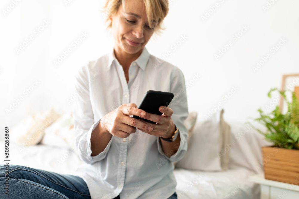 Mature woman sitting on bed at home using smartphone Mature woman sitting on bed at home using smartphone