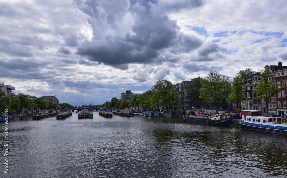 Amsterdam, Holland, August 2019. View of the river on the Amstel river, outskirts of the city. Big boats moored on a sunny day with blue sky and white clouds.
