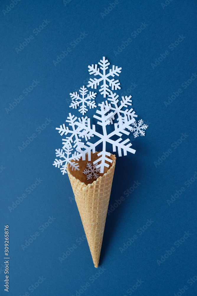 Waffle cone with paper snowflakes on blue background. Holiday concept.