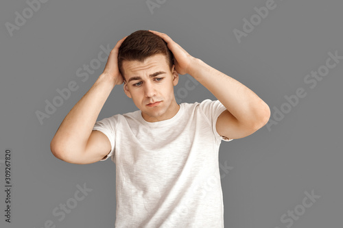 Freestyle. Young man standing isolated on grey holding head upset