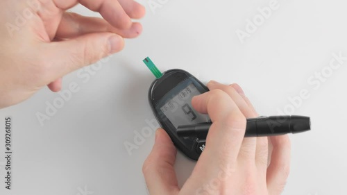 An unrecognized person measures blood glucose with a glucometer. Squeezes a drop of blood and puts a single strip test. Measuring 6.2 mmol. Concept prevention of diabetes