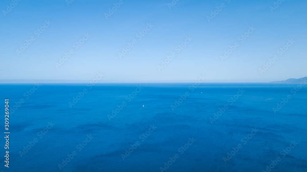 View of the blue azure ocean in which a white sailing boat floats. Drone shooting from above.