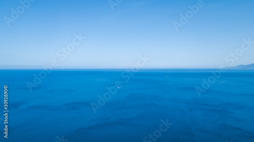 View of the blue azure ocean in which a white sailing boat floats. Drone shooting from above.