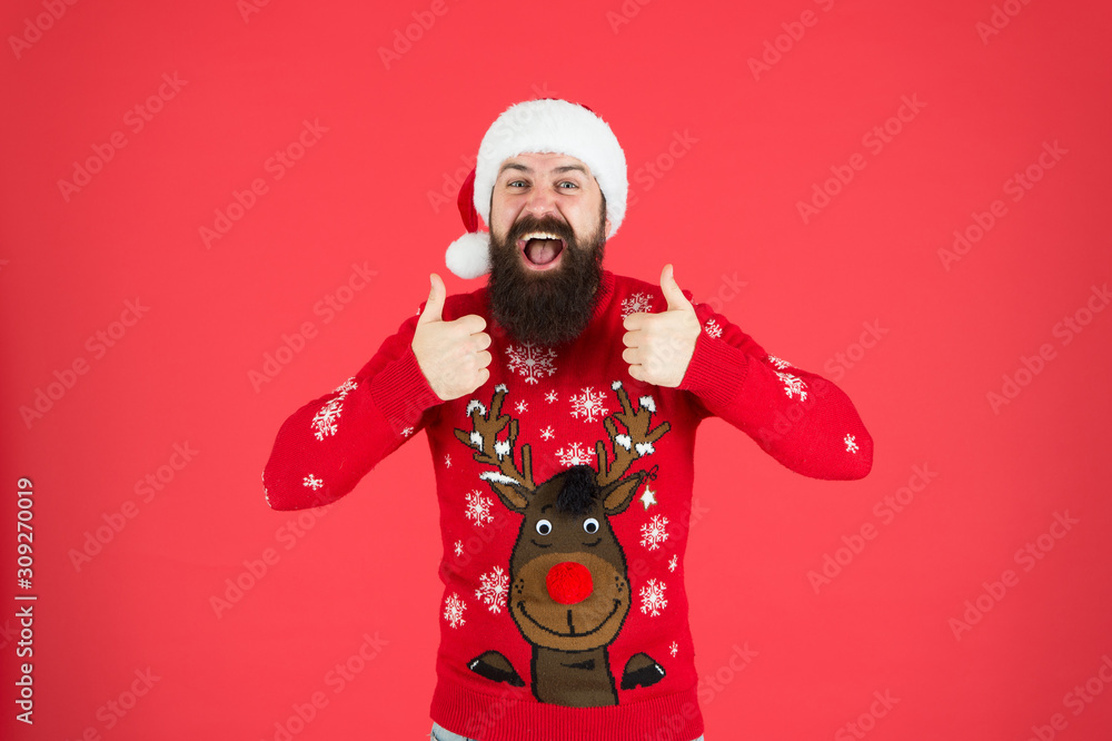 Happy Holiday Season. male at xmas party. happy new 2020 year. funny hipster sweater. knitwear fashion. winter holiday celebration. feel hapiness. bearded man santa hat red wall. christmas time