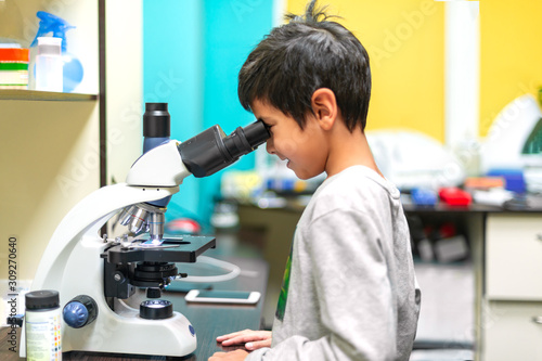 The schoolboy looks through a microscope in a laboratory with curiosity.  Children came on an excursion to the clinic.
