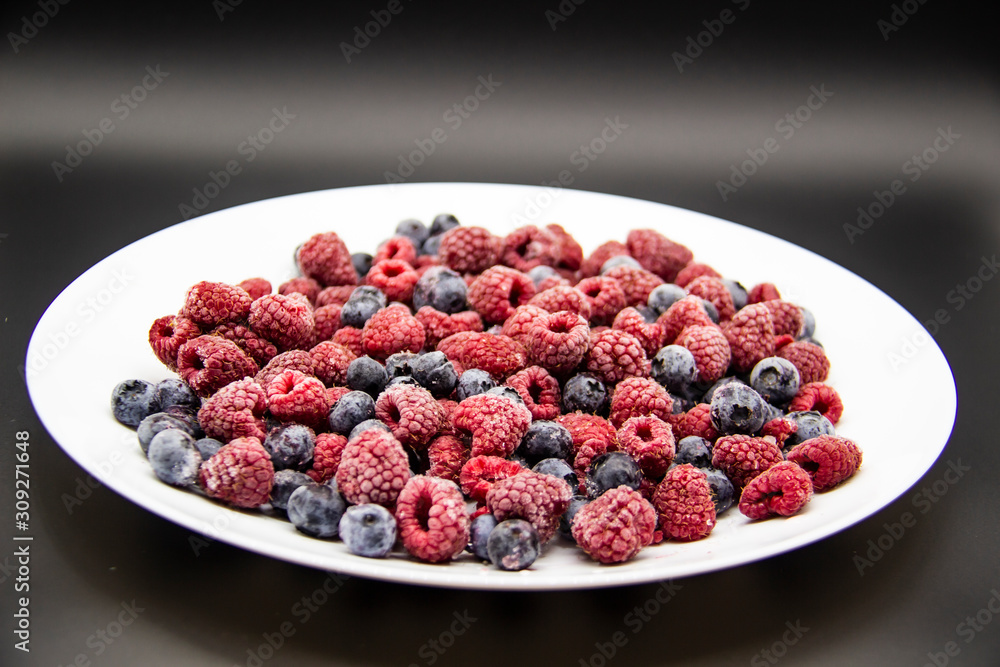 A Berry mix from frozen raspberries and blueberries on the white plate. A Frozen Berries in black background. A sweet background with frozen raspberries and blueberries A Berry mix from frozen raspberries and blueberries on the white plate. A Frozen Berries in black background. A sweet background with frozen raspberries and blueberries