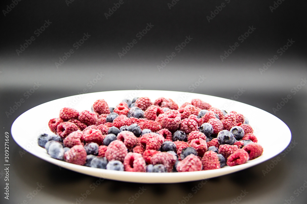 A Berry mix from frozen raspberries and blueberries on the white plate. A Frozen Berries in black background. A sweet background with frozen raspberries and blueberries A Berry mix from frozen raspberries and blueberries on the white plate. A Frozen Berries in black background. A sweet background with frozen raspberries and blueberries