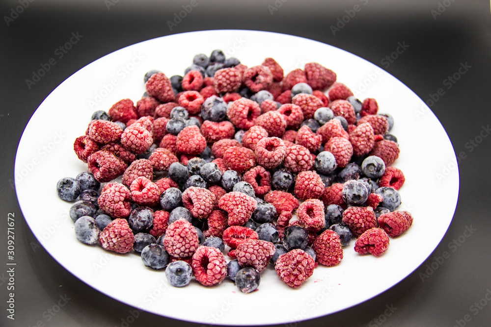 A Berry mix from frozen raspberries and blueberries on the white plate. A Frozen Berries in black background. A sweet background with frozen raspberries and blueberries A Berry mix from frozen raspberries and blueberries on the white plate. A Frozen Berries in black background. A sweet background with frozen raspberries and blueberries