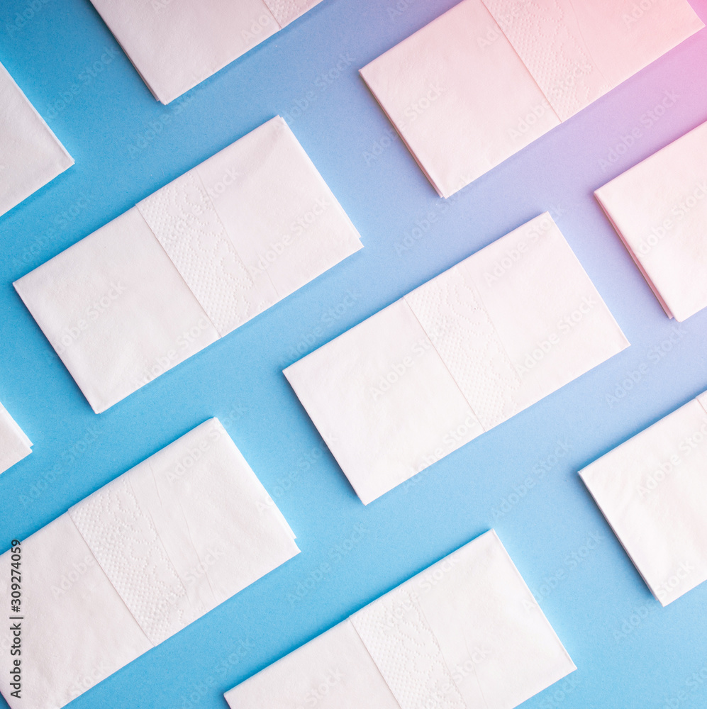 White hygiene napkins on a blue background. Skincare mockup for design. Stack of disposable napkins. Cosmetology concept. White hygiene napkins on a blue background. Skincare mockup for design. Stack of disposable napkins. Cosmetology concept.