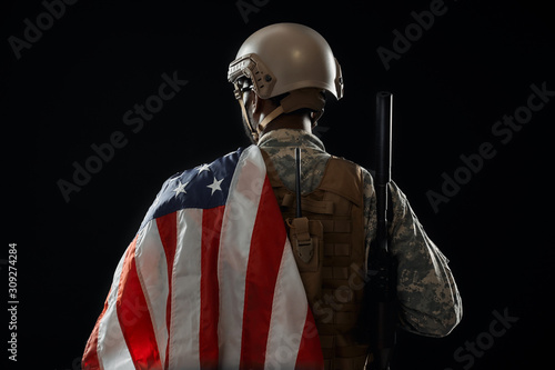 Incognito soldier holding American flag on shoulder.