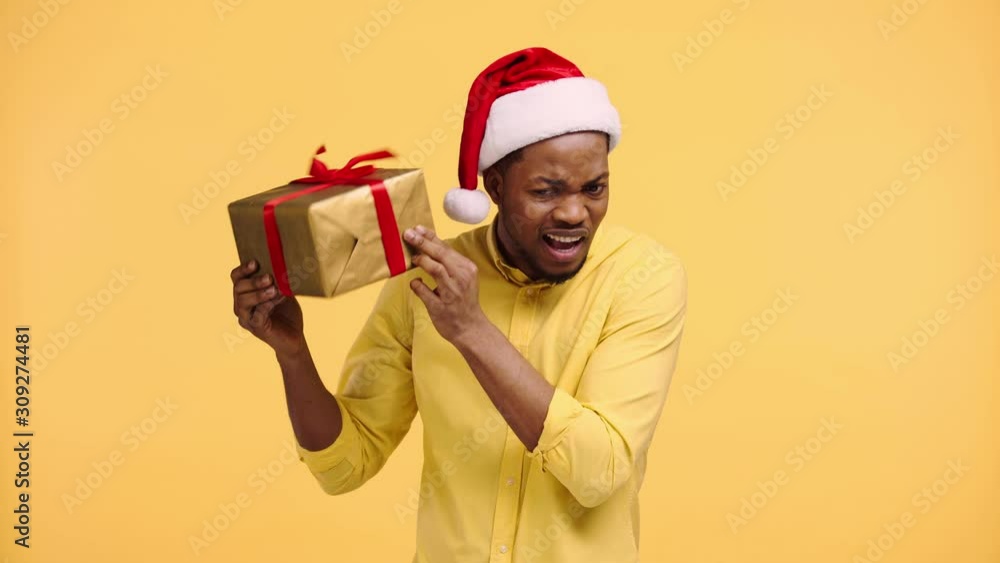 curious african american man shaking gift box isolated on yellow curious african american man shaking gift box isolated on yellow