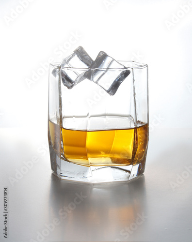 Studio isolated splashing whiskey over white background. Two ice cubes fall into a glass of whiskey