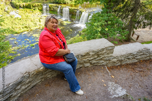 Mature plump woman in red resting at the waterfall
