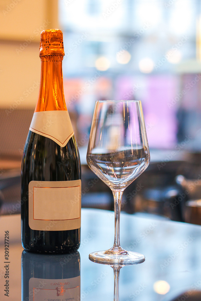 champagne bottle with blank labels on reflective table near an empty glass in a restaurant lights