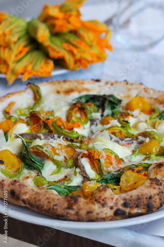 detail of a pizza with zucchini flowers, fresh mozzarella cetara anchovies, parmesan cheese and yellow tomatoes of Vesuvius