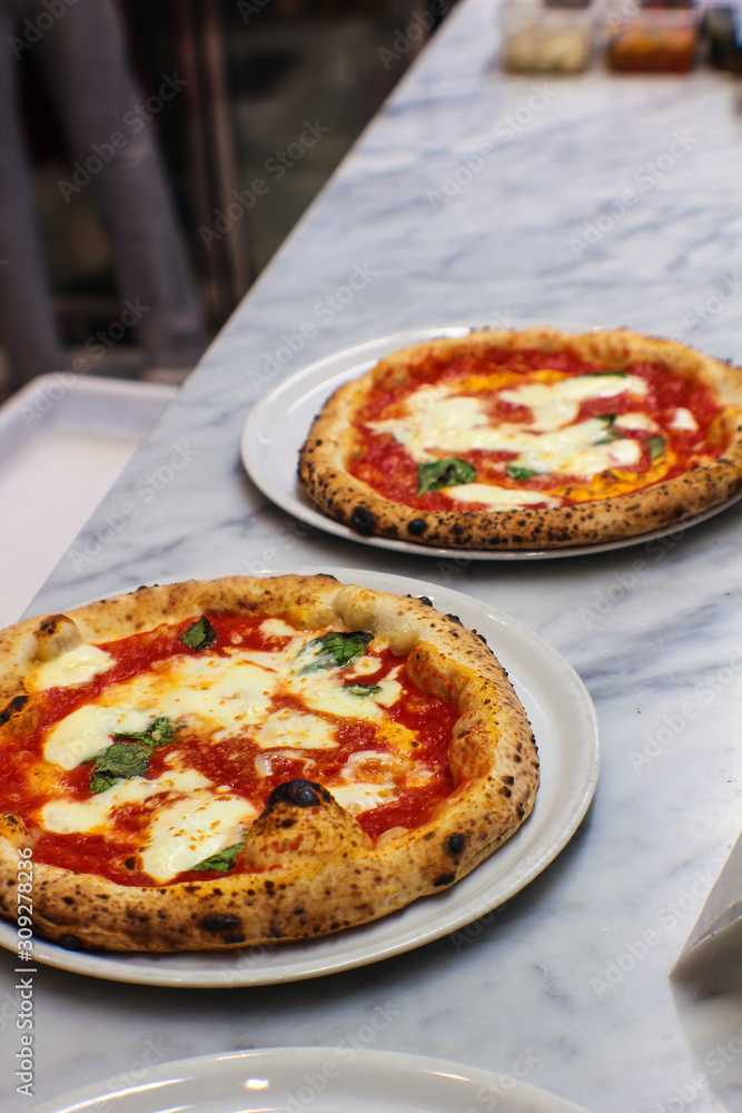 two margherita pizzas freshly baked on the pizzaiolo's work table