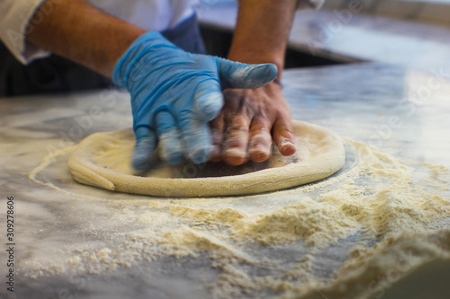hands of pizza maker knead the dough for pizza with flour on a marble top of an Italian pizzeria