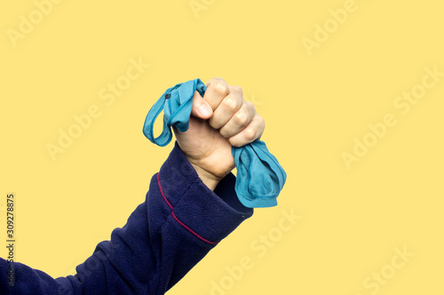 Concept of man that owns a woman, man who possess a woman, bad relationship, conflictual relationship. Hand holding an aqua menthe tanga in a sign of possession. Yellow background