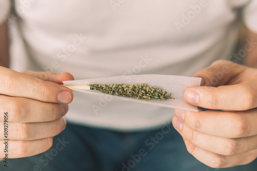 Man preparing and rolling marijuana cannabis joint. Close up of marijuana joint with grinder. marijuana use concept. Man rolling a cannabis joint on white background.