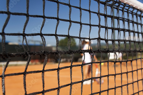 Tennis court with net and blue sky in the background. Focus on the net, close up. 