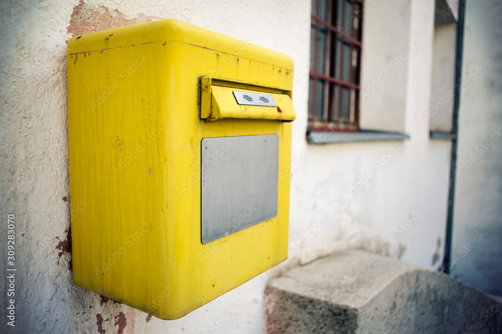 A bright old yellow post box on the wall, close up.