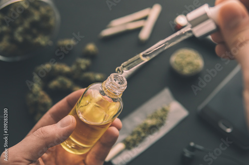 natural herb, CBD cannabis OIL. hemp product, Hand holding bottle of Cannabis oil in pipette, medical marijuana concept, close up,