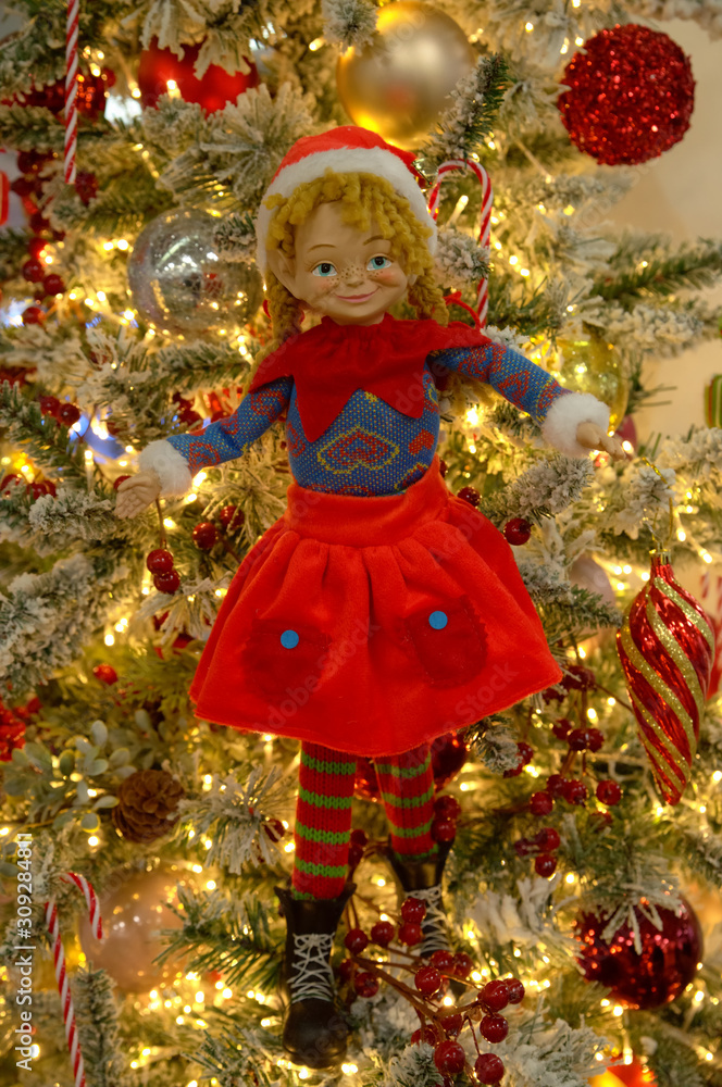 Toy girl Elf, bright garland and Christmas decoration hanging on a on the branches of a Christmas tree. Shallow depth of field. New Year and holiday concept. Toy girl Elf, bright garland and Christmas decoration hanging on a on the branches of a Christmas tree. Shallow depth of field. New Year and holiday concept.