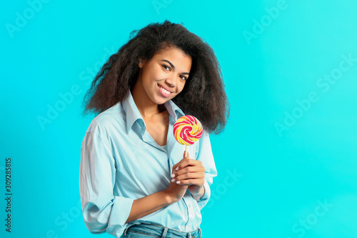 Happy African-American woman with tasty lollipop on color background