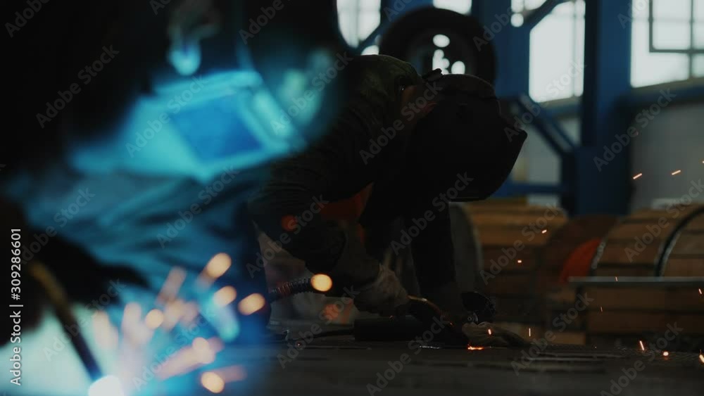 builders in protective wear weld parts on floor in workshop builders in protective wear weld parts on floor in workshop