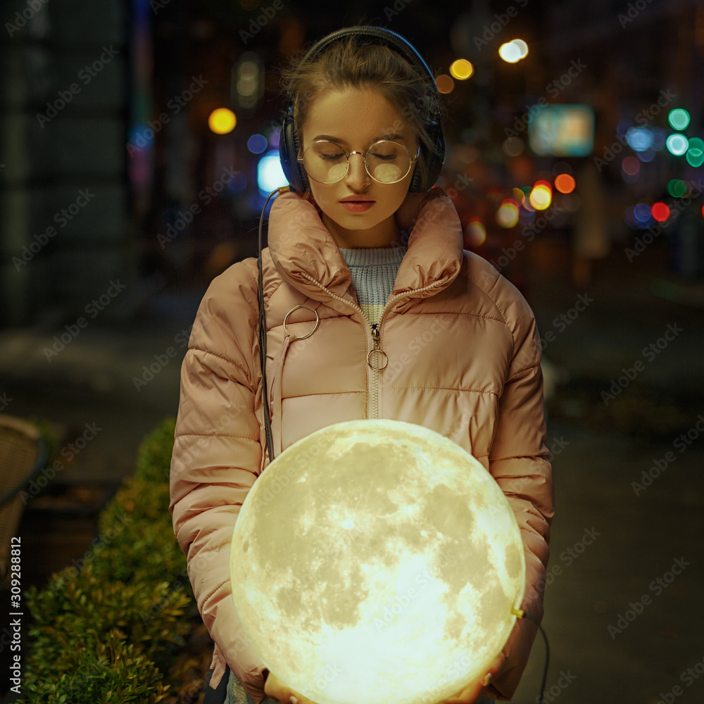 Naklejka premium Romantic portrait of a young girl on the street of the evening city with the moon in her hands