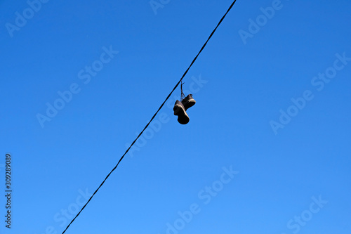 An old pair of men's sneakers hanging on wires against a blue sky. Torn black sneakers on a wire.