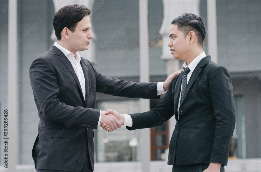 smiling businessmen shaking hands together while standing infront their new modern office