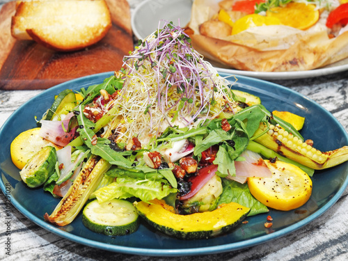 Warm salad with roasted vegetables with spices and sauce on a blue plate.