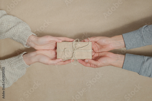 Giving away a gift in brown paper on matching background. Concept of reducing carbon footprint in everyday lifestyle and nature friendly trends