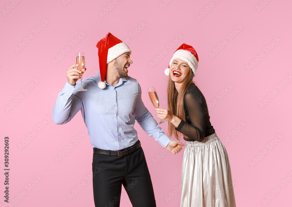 Obraz premium Happy couple in Santa Claus hats and with glasses of champagne on color background