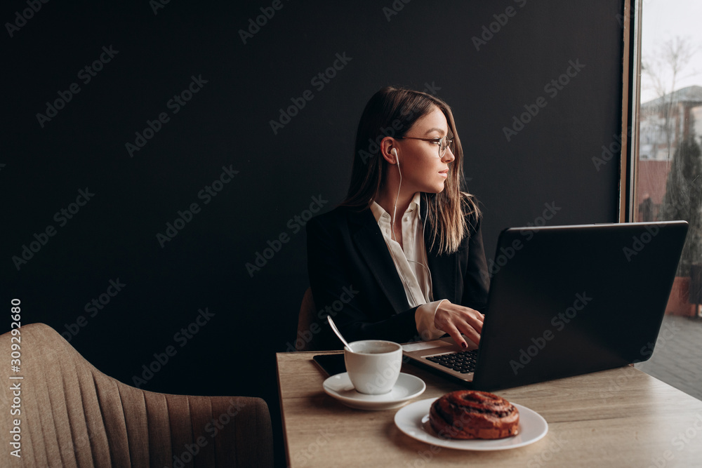 a beautiful girl wearning in office clothes and sunglasses listening music with headphones and working on the laptop in the cafe a beautiful girl wearning in office clothes and sunglasses listening music with headphones and working on the laptop in the cafe