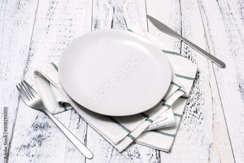 White Plate with utensils and dish towel on white wooden background side view