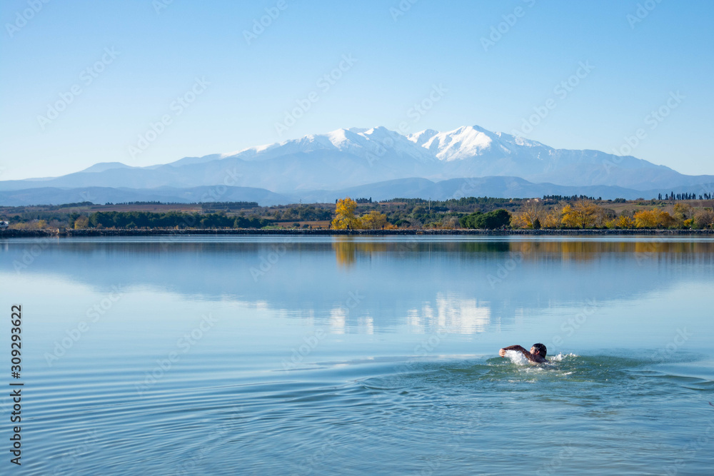 Man swimming in a lake with mountains in the background. Swimming in nature. Lake of Villeneuve-de-la-Raho (France) overlooking the Pyrenees and the Canigo