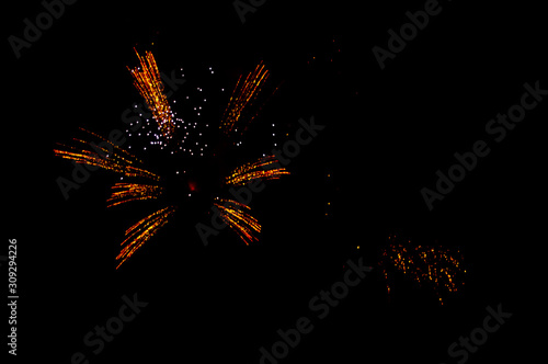 Yellow and red fireworks in the shape flower on the left side on a black background.