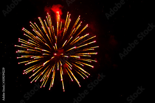 Yellow and red fireworks in the shape sphere on the left side on a black background.