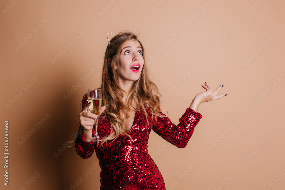 Emotional woman with glass of champagne telling something and waving hand. Sensual girl in red sparkle dress looking up with interested face expression, posing at party. Emotional woman with glass of champagne telling something and waving hand. Sensual girl in red sparkle dress looking up with interested face expression, posing at party.