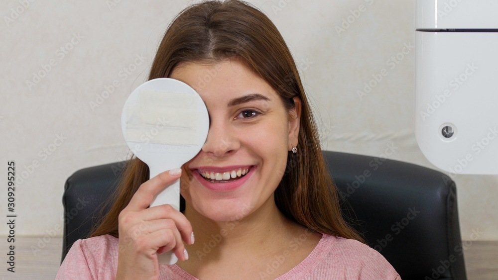 Ophthalmology treatment - young smiling woman checking her visual acuity - closing her eye with an eye shield and saying what the projection says