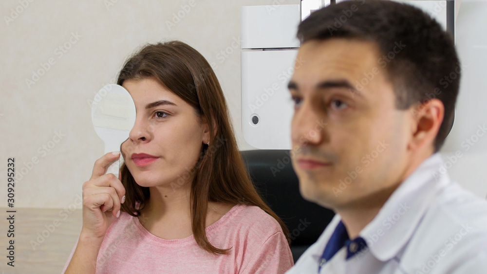 Ophthalmology treatment - young woman checking her visual acuity closing her eye with an eye shield Ophthalmology treatment - young woman checking her visual acuity closing her eye with an eye shield