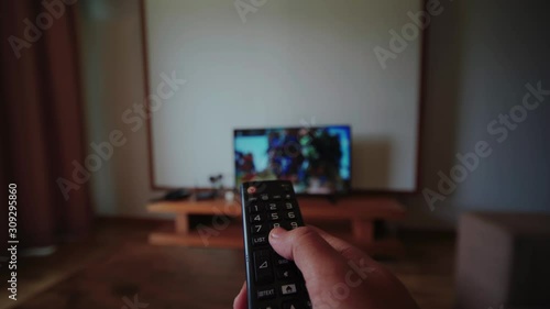 Hand holding tv remote control, changing channel on television, watching movie at living room in house, chilling alone.