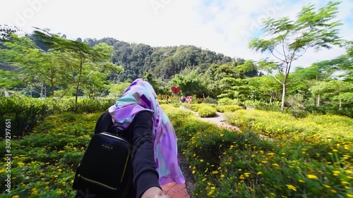 Attractive young Muslim woman holding hand with lover or boyfriend or husband, enjoying view of green park with beautiful flowers at Cameron Highlands, Pahang in slow motion.