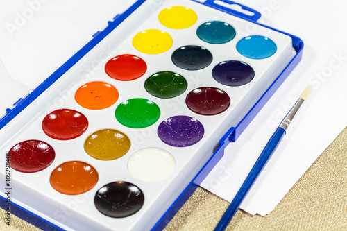 A new box with multi-colored paints and a brush for painting. Diagonally
