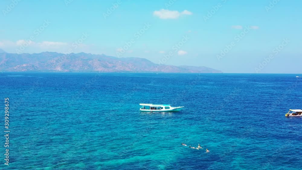Aquamarine sea surface reflecting sunlight of bright blue sky over mountains of tropical islands, tourists swim near anchored boat on shallow lagoon Aquamarine sea surface reflecting sunlight of bright blue sky over mountains of tropical islands, tourists swim near anchored boat on shallow lagoon