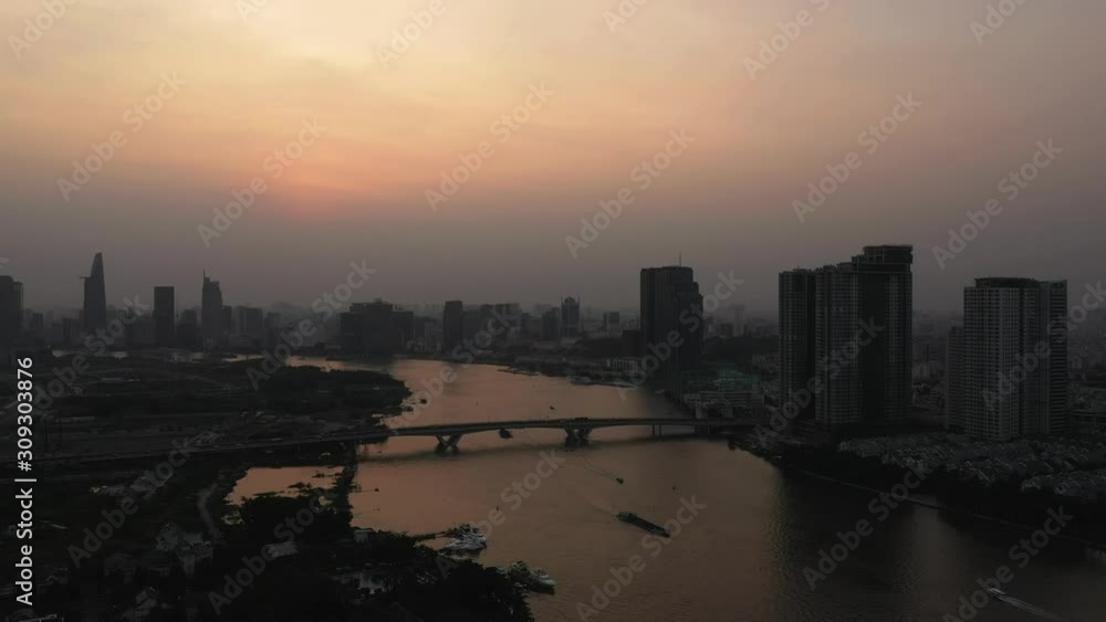 Drone shot of Saigon river smoggy sunset typical of a day with an extreme air pollution reading in Southeast Asia. Camera locked off as freighters move along the river. The skyline is visible Drone shot of Saigon river smoggy sunset typical of a day with an extreme air pollution reading in Southeast Asia. Camera locked off as freighters move along the river. The skyline is visible